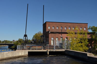 Bridge over river by buildings against clear blue sky