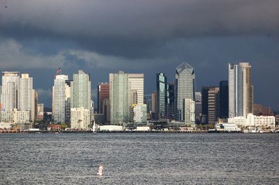 Sea by modern buildings against sky in city