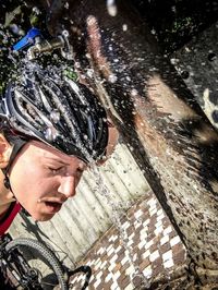 Male cyclist washing head below faucet