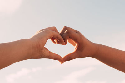 Two sisters joining hands in the shape of a heart in the background of the blue sky, family