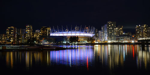 Illuminated city by river against sky at night