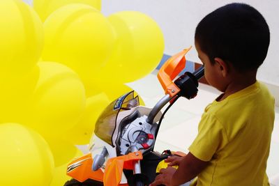 Boy sitting on toy motorcycle by balloons