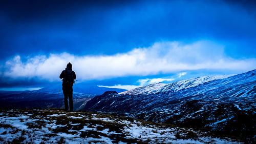 Rear view of silhouette man standing on snowcapped mountain against sky