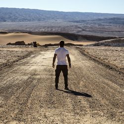 Rear view of mid adult man standing on dirt road at desert