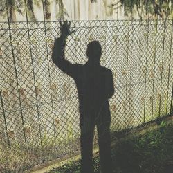 Shadow of silhouette man standing on chainlink fence