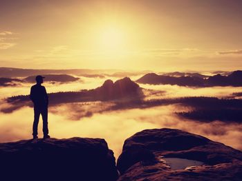 Silhouette man standing on rock against sky during sunset