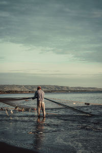 Rear view of man standing at beach against sky