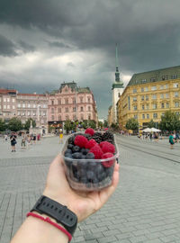 Midsection of person holding ice cream against sky in city