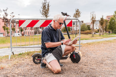 Commuter hipster man with electric scooter using smartphone in the suburbs. eco transport concept 