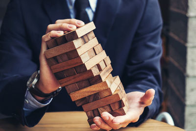 Midsection of businessman holding stacked wooden toy blocks on table