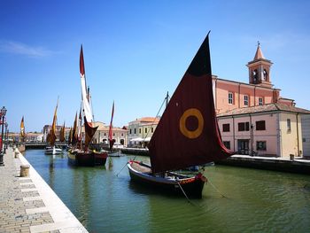 Sailboats moored on canal amidst buildings in city against sky