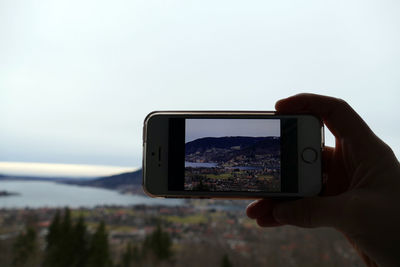 Man photographing through smart phone against sky