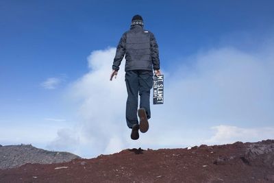 Low angle view of man with signboard jumping against sky