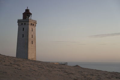 Lighthouse by sea against sky during sunset