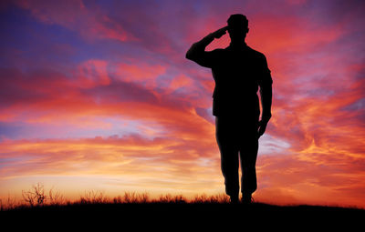 Silhouette man standing on field against orange sky