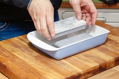 Midsection of man holding sharpening stone over container on table