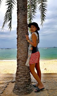 Full length portrait of young woman standing by tree at beach