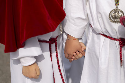 Midsection of men wearing religious dress while holding hands outdoors