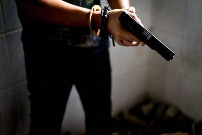 Midsection of man holding gun while standing at home