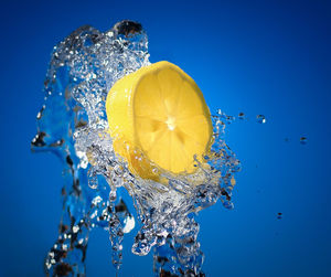 Close-up of lemon splashing water against blue background