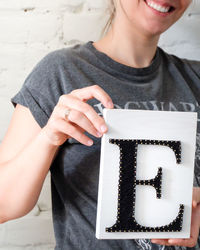 Midsection of smiling woman with letter e standing against wall