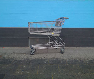 Empty shopping cart on sidewalk by blue wall