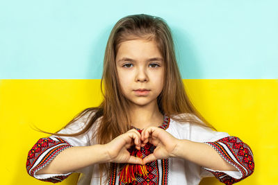 Portrait of young woman standing against yellow background
