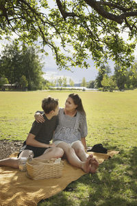 Mother with son sitting on picnic blanket  barefoot
