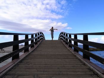 Man standing on footbridge against sky