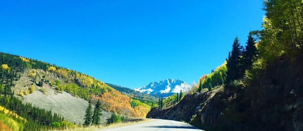 Road amidst snowcapped mountains against clear blue sky