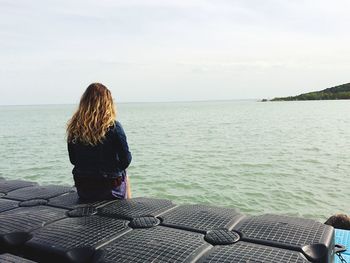 Rear view of woman sitting on pier at lake balaton against sky