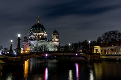 Illuminated buildings by river against sky in city at night