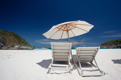 Deck chairs on beach against clear blue sky