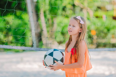 Cute girl holding volleyball standing by net