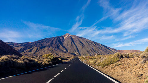 Empty road leading towards mountain against sky