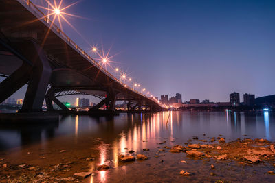 Illuminated bridge over river against sky at night