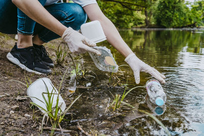Low section of female volunteer cleaning plastic waste from pond at park