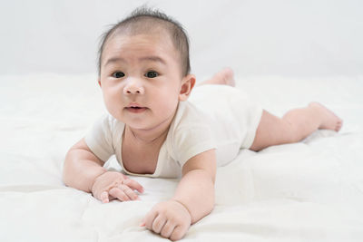 Training tummy time of adorable young asian newborn little baby boy prone on the bed.