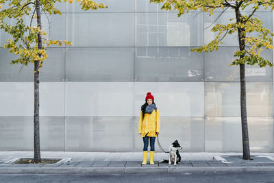 Smiling woman standing with dog on footpath during autumn
