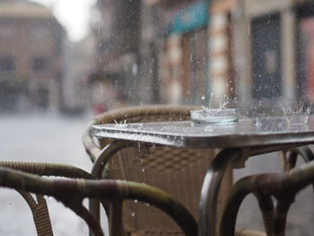 Raindrops making water crown on table by chairs at sidewalk cafe in city