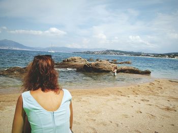 Rear view of woman looking at boy playing in sea against sky