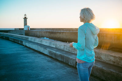 Woman walking on promenade against sky during sunset