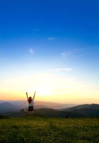 Man sitting on field against sky during sunset