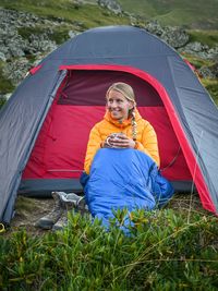 Young woman sitting in front of a tent in a sleeping bag.