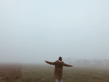Rear view of man with arms outstretched on field against sky
