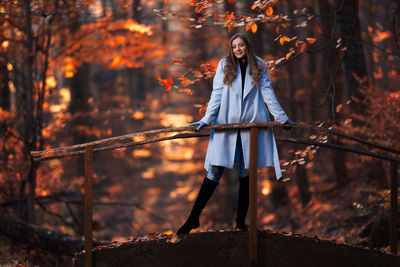 Full length of woman standing by trees in forest during autumn