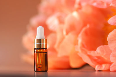 Cosmetic amber glass dropper bottle on stone podium with peonies in soft focus. oil, serum, fruit