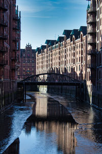 Bridge over river by buildings against sky