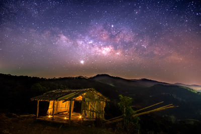 Illuminated broken house on mountain against star field sky