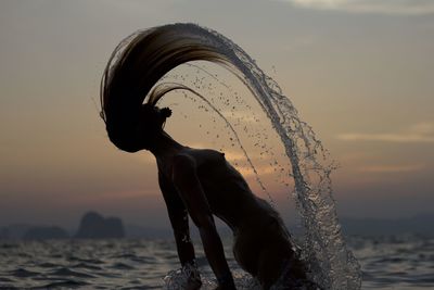 Man splashing at beach against sky during sunset